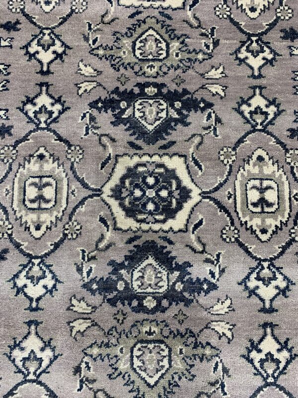 Low-pile rug detail showing a traditional medallion pattern in navy, cream, and medium grey on a mauve field.