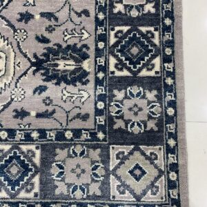 Lavender rug corner showing a dense pile, traditional navy floral pattern, and geometric block borders.