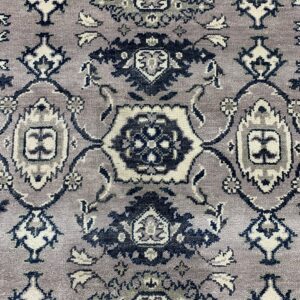Textured pile rug detail showing a traditional pattern in dusty purple, cream, dark gray, and navy blue.
