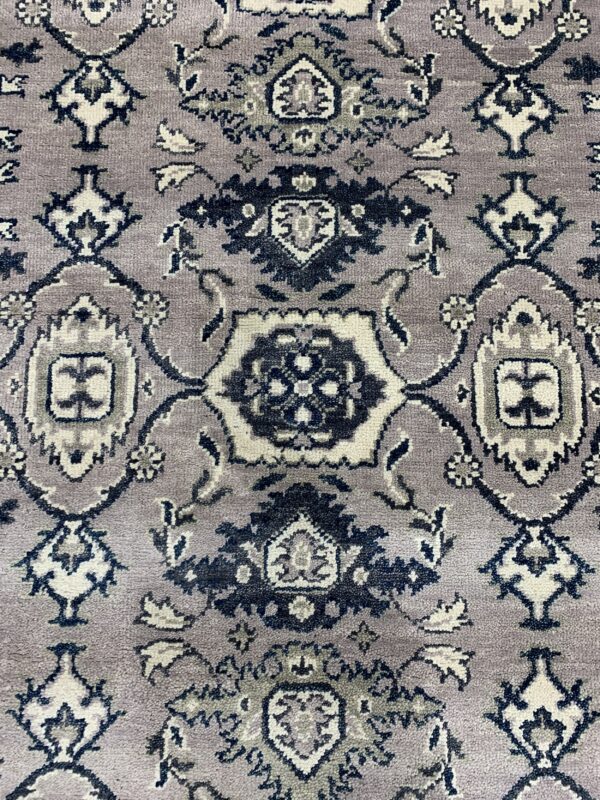 Textured pile rug detail showing a traditional pattern in dusty purple, cream, dark gray, and navy blue.