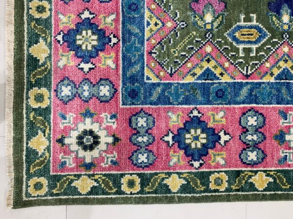 Detailed traditional rug corner with pink, blue, green, and yellow geometric patterns resting on a white tiled floor.