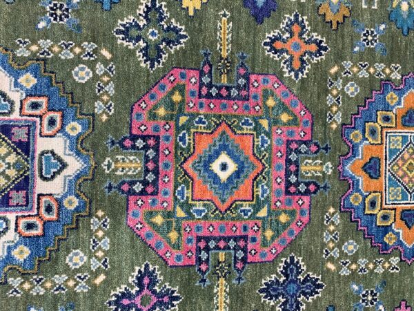 A close-up of a dense green rug with a vibrant pink, blue, and orange geometric medallion pattern.