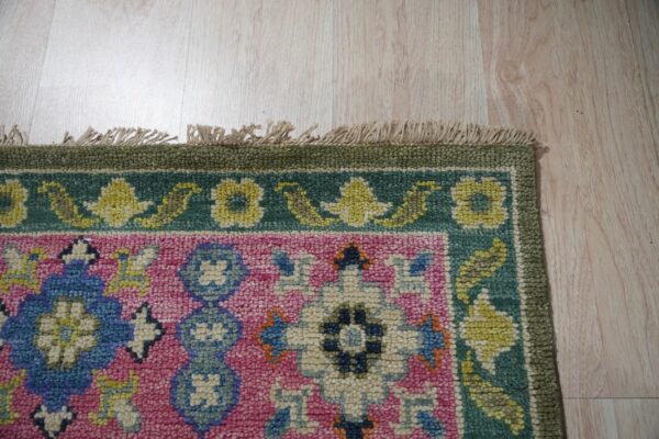 Colorful pink, blue, and green textured rug with floral patterns and visible fringe rests on light wood flooring.