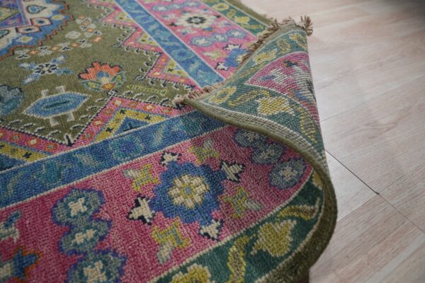 Curled traditional rug with olive green, bright pink, and blue geometric patterns on light wood floors.