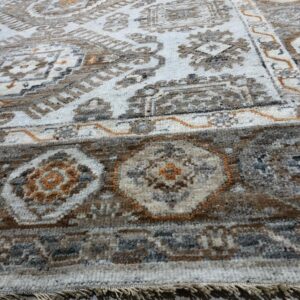 Close-up of a white rug with distressed brown, gray, and rust geometric patterns and fringe on wood flooring.