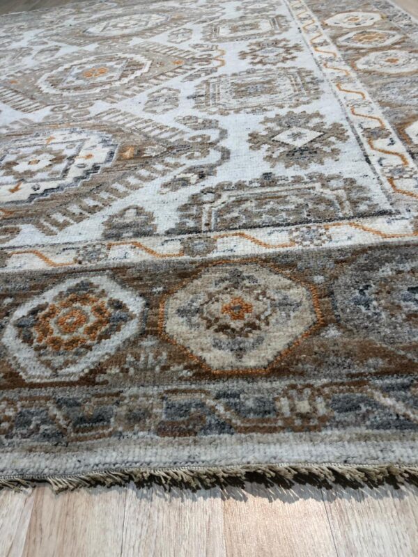 Close-up of a white rug with distressed brown, gray, and rust geometric patterns and fringe on wood flooring.