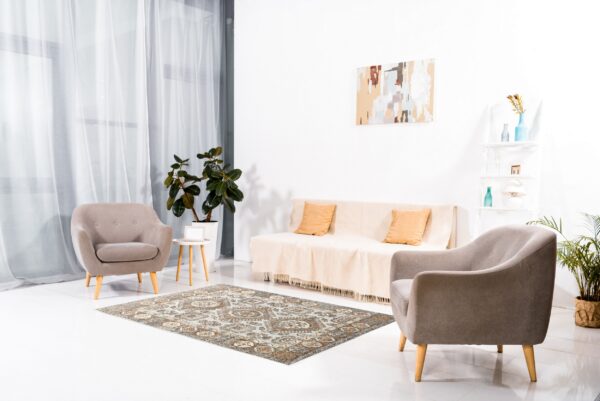 An intricate, traditional rug in rust and gray tones rests on glossy white flooring between modern chairs.