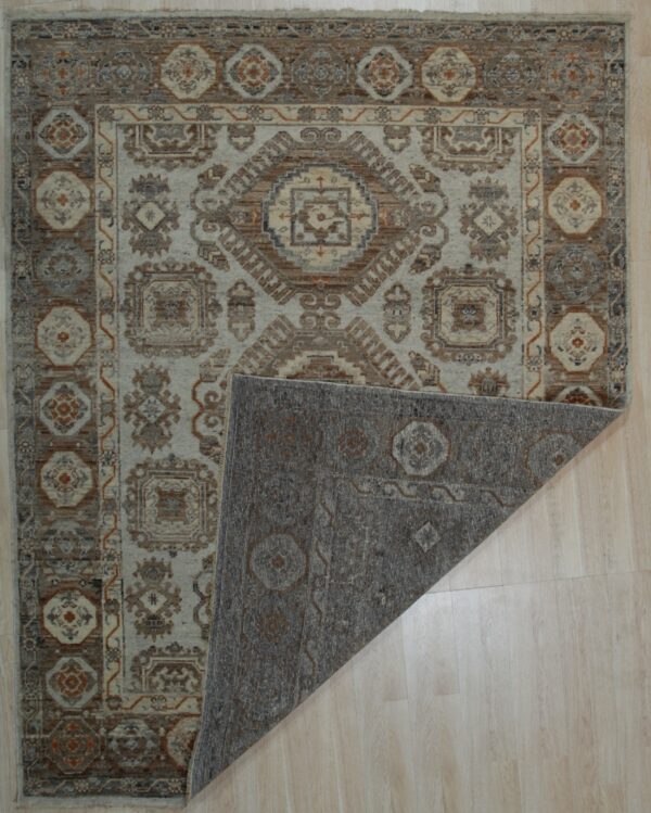 Beige and brown traditional area rug on a light floor, showing the gray patterned backing folded over.