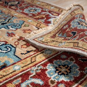 A patterned rug in rust, blue, and beige is partially rolled up on light wood plank flooring.