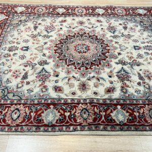 Cream and red traditional rug with a detailed central medallion rests on light hardwood planks.