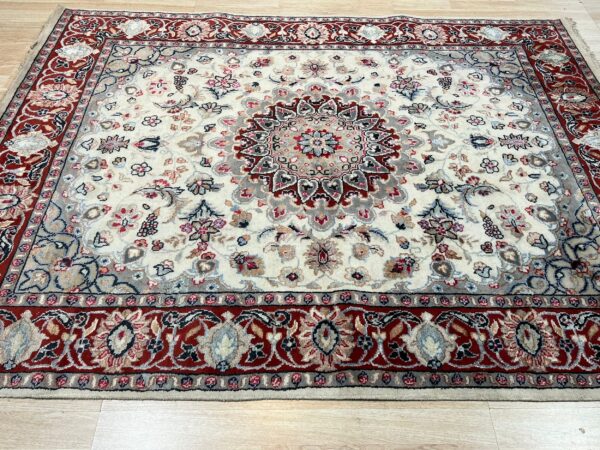Cream and red traditional rug with a detailed central medallion rests on light hardwood planks.