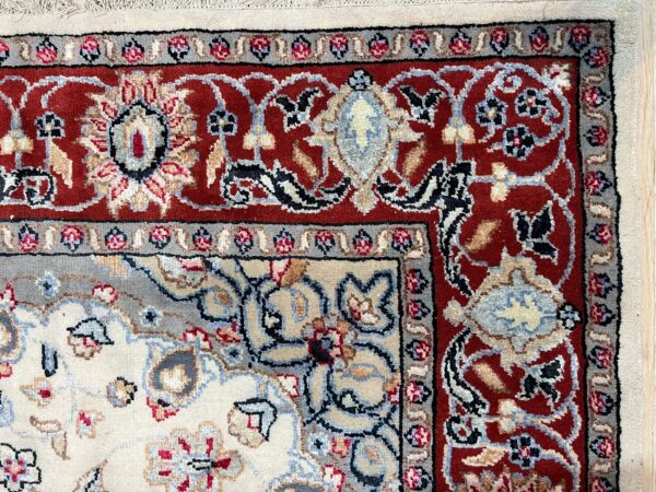 Close-up of a rug corner showing intricate floral patterns in red, cream, blue, and gray colors.