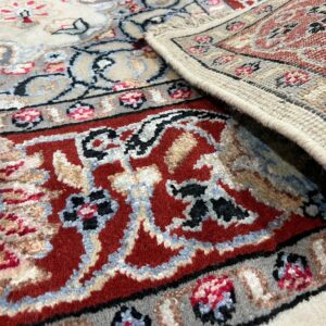 Traditional red and cream patterned rug folded over, revealing its woven backing and fringe.