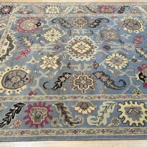 Blue area rug with a traditional pattern of yellow, gray, and purple florals on light wood flooring.