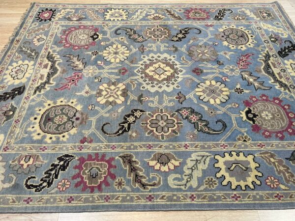 Blue area rug with a traditional pattern of yellow, gray, and purple florals on light wood flooring.