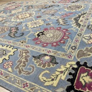 Blue traditional rug with floral patterns in cream, gray, and magenta, resting on a wood floor.