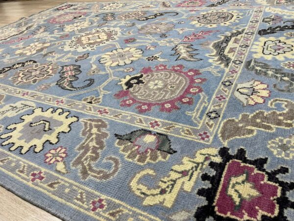 Blue traditional rug with floral patterns in cream, gray, and magenta, resting on a wood floor.