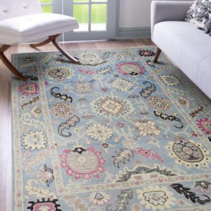 A light blue low-pile rug with pink, cream, and gray floral patterns rests on wood floors near modern furniture.