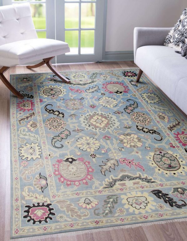 A light blue low-pile rug with pink, cream, and gray floral patterns rests on wood floors near modern furniture.