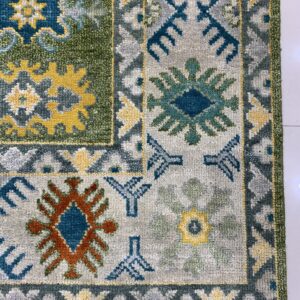 A textured rug with tribal geometric patterns in green, light gray, blue, yellow, and rust colors.