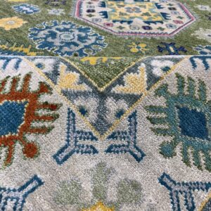 Coarse pile rug detail showing a fold, featuring blue, yellow, green, and grey stylized medallions and geometric motifs.