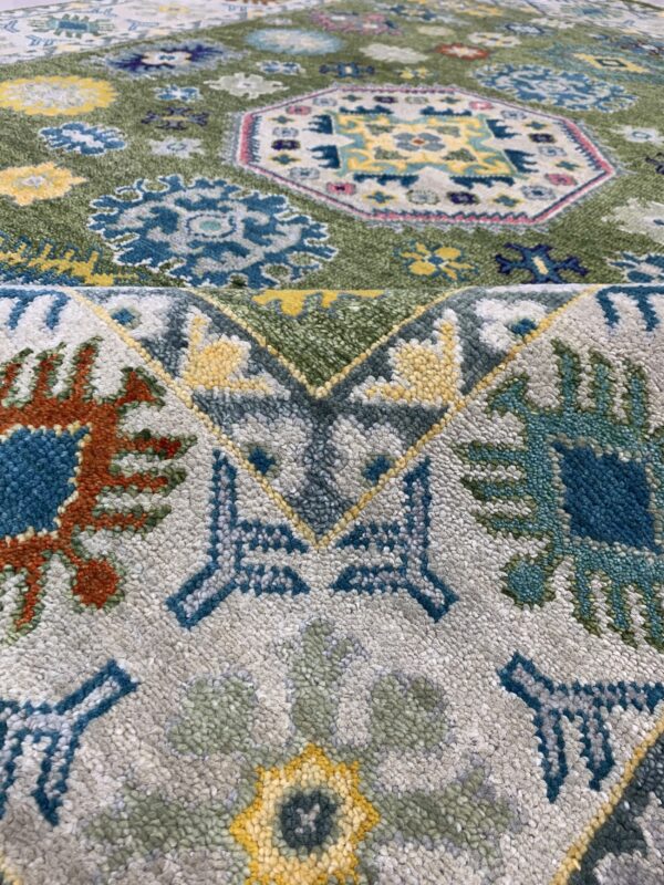 Coarse pile rug detail showing a fold, featuring blue, yellow, green, and grey stylized medallions and geometric motifs.