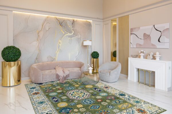 Geometric green rug under a curved pink sofa and gold decor on white marble flooring.