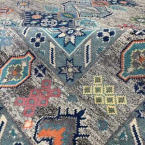 High-pile rug featuring a distressed geometric pattern in gray, teal, navy, orange, and dusty pink.