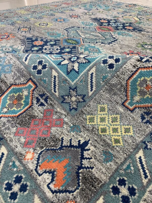 High-pile rug featuring a distressed geometric pattern in gray, teal, navy, orange, and dusty pink.