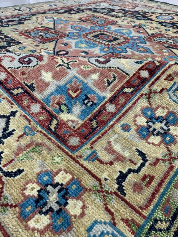 Detailed view of a folded, thick-pile rug featuring traditional motifs in tan, blue, red, pink, and navy.