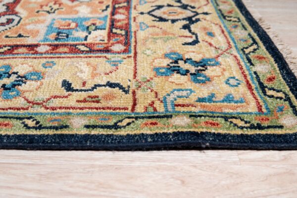 Medium pile rug with traditional yellow, red, blue, and green motifs resting on light wood flooring.