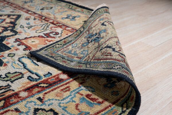 A multicolored traditional patterned rug is curled back, revealing the intricate backing on light wood floors.