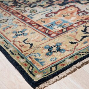 Beige rug with traditional blue, rust, and navy patterns shown close-up on pale wood planks.