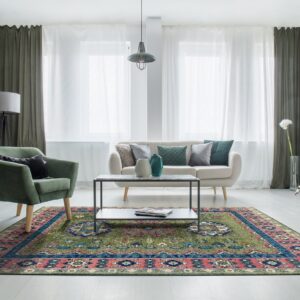 A traditional green, blue, and pink patterned rug anchors a living room with a cream sofa and green chair.