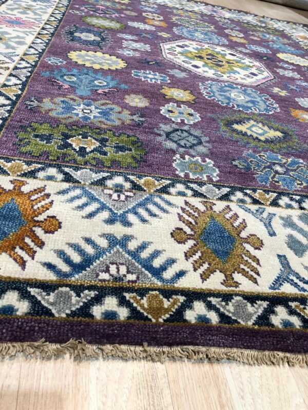 Textured purple rug featuring colorful floral and geometric patterns with a wide cream and navy blue border.