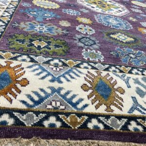 Textured purple rug displaying multicolor medallions and a wide white border with blue tribal patterns on wood flooring.