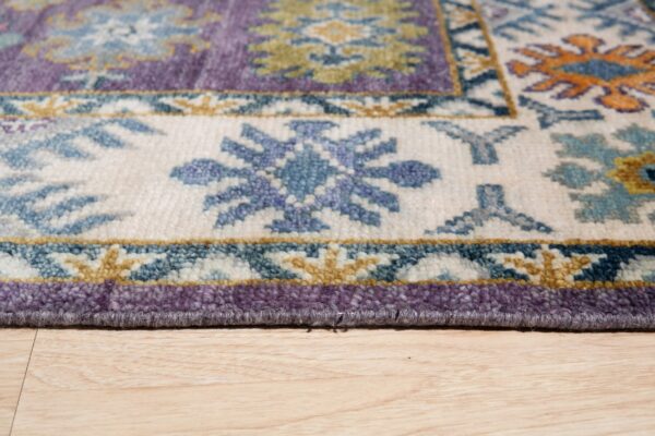 Textured purple, blue, and cream traditional rug border on light hardwood flooring.
