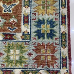 Geometric rug close-up in rust, teal, dark blue, and yellow with a chunky texture on white flooring.