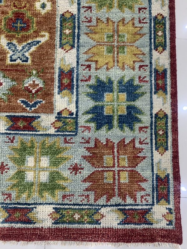 Geometric rug close-up in rust, teal, dark blue, and yellow with a chunky texture on white flooring.