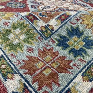 Textured rug displaying geometric and floral patterns in red, light blue, rust, and forest green.