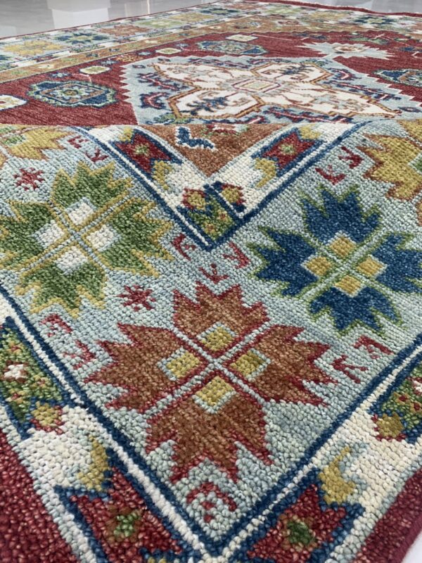 Textured rug displaying geometric and floral patterns in red, light blue, rust, and forest green.