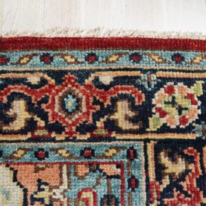 Red and navy high-pile rug with a detailed geometric border rests on light wood flooring.