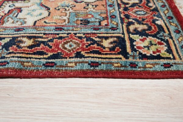 Ornate navy, terracotta, and teal patterned rug edge with a dense low pile rests on pale wood planks.