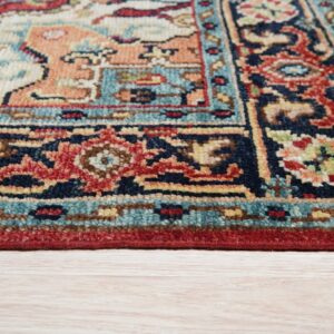 Traditional rug corner displaying red, navy, peach, and teal geometric patterns on light wood flooring.