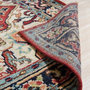 Multi-colored traditional rug with red edging is partially folded back, resting on light wood plank flooring.
