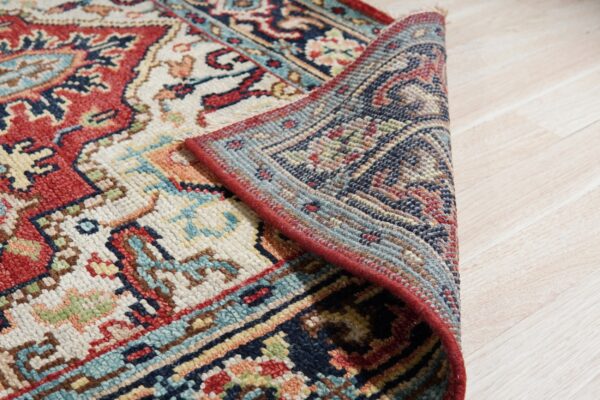 Multi-colored traditional rug with red edging is partially folded back, resting on light wood plank flooring.