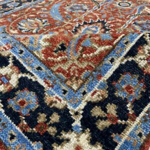 Textured traditional rug displaying intricate patterns in rust, navy, and light blue on shiny white tile flooring.