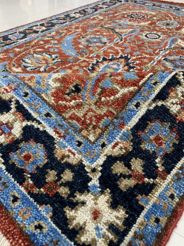 Textured traditional rug displaying intricate patterns in rust, navy, and light blue on shiny white tile flooring.