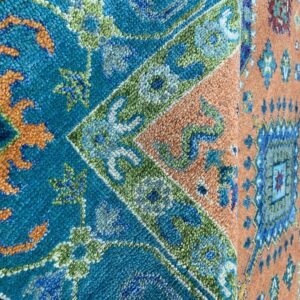 Close-up of a rug featuring detailed traditional patterns in teal, orange, blue, and green high pile.
