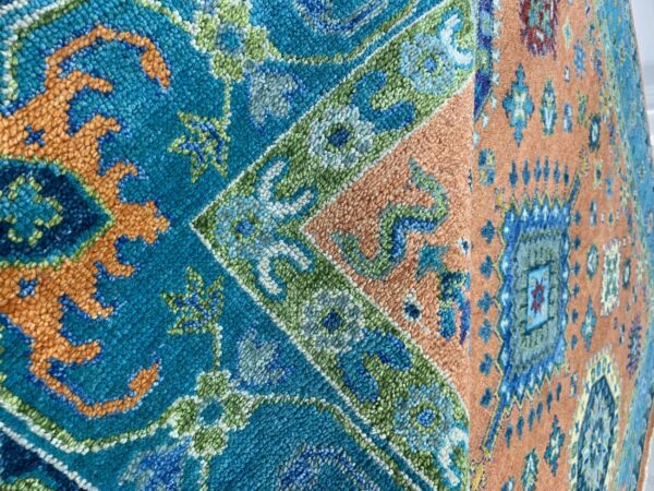 Close-up of a rug featuring detailed traditional patterns in teal, orange, blue, and green high pile.